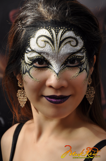 Woman with a white upper mask outlined in black with gold dots